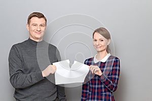 Studio shot of adult couple holding and tearing paper sheet