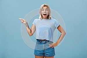 Studio shot of amazed impressed good-looking sportswoman in trendy t-shirt with tattoos opening mouth with enthusiasm