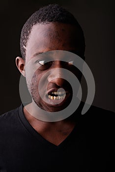 Studio shot of angry young black African man screaming in dark r