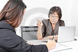 Studio shot of Asian, senior businesswoman with laptop, sitting with two young staffs in board room in office, boss making serious photo