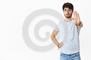Studio shot of attracitve young masculine male with blue eyes and bristle pulling palm at camera in stop and prohibition