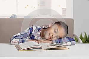 Studio shot of attractive little girl of mulatta with braids of frizzy. The girl sits at the table and study