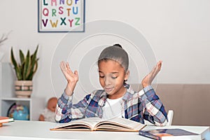 Studio shot of attractive little girl of mulatta with braids of frizzy. She reads the textbook and does not understand the text