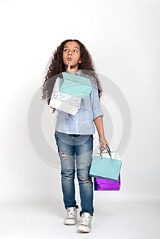 Studio shot of attractive little girl of mulatta with long frizzy. She goes shopping in paper shopping bags and puzzles her