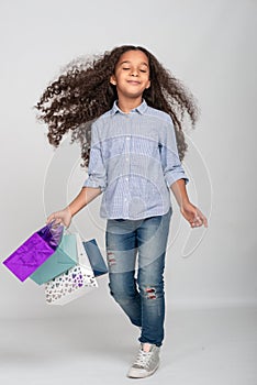 Studio shot of attractive little girl of mulatta with long frizzy. She has fun with paper bags from shopping, eyes closed from
