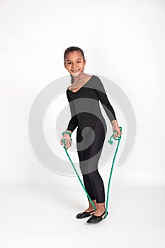Studio shot of attractive little gymnast girl of mulatta wearing black leggings and a bathing suit with a green jump rope on a