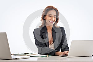 Studio shot of an attractive mid aged woman sitting at desk and using laptop against isolated white background