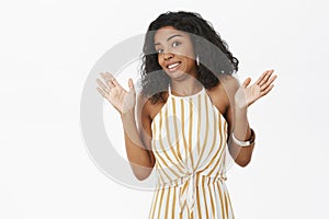 Studio shot of awkward displeased funny dark-skinned woman raising palms in surrender and shrugging smiling with fake