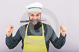 Studio shot of a bearded man holding a sharp knife with his teeth