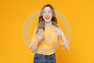 Studio shot of Beautiful Asian woman holding smartphone and smiling on light yellow background