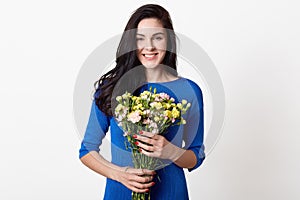 Studio shot of beautiful brunette girl holding bouquet of flowers, attractive woman with big bunch of flowers, dark haired female