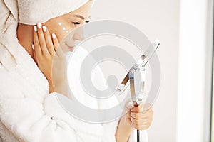 Studio shot of beautiful young woman applying moisturizer cream onto her face