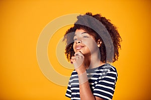 Studio Shot Of Boy With Puzzled Expression Thinking Against Yellow Background