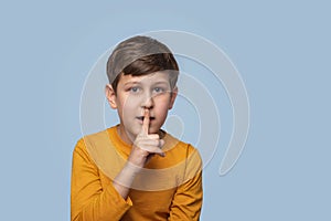 Studio shot of a boy showing a gesture of secrecy by touching the index finger to his lips ,  on blue