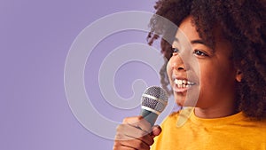 Studio Shot Of Boy Singing Karaoke Into Microphone Against Purple Background