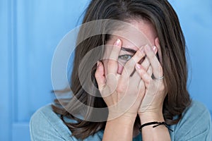 Studio shot of brunette girl hiding eyes under hand while feeling ashamed.