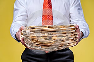Studio shot of businessman or accountant holding pile of papers. Yellow background