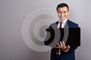 Businessman wearing suit while holding laptop against gray backg