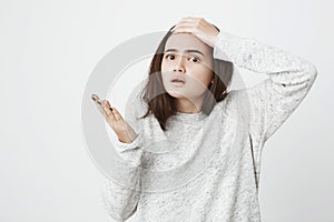 Studio shot of caucasian female student in despair and shock, holding hand on forehead and gesticulating while standing