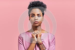 Studio shot of cheerful African American female keeps hands together near chin, smiles broadly, anticipates for surprise