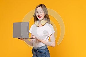 Studio shot of cheerful beautiful Asian woman in white t-shirt and holding laptop mockup of blank screen on yellow background