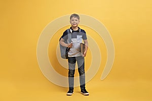 Studio shot of cheerful cute boy schooler posing on yellow