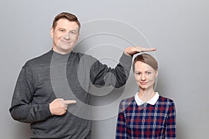 Tall man is showing height of short woman and pointing at her