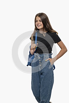 Studio shot of  cheerful teenager girl with braces  walking with a backpack on  shoulder and holding hand in  pocket, isolated