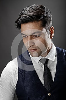 Studio shot of cheerful, young, handsome Indian male model in formal wear wearing white shirt, black tie, black coat against grey