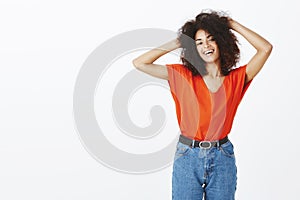 Studio shot of chill outgoing african american woman with afro hairstyle holding hands on back of head and gazing at