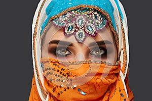 Studio shot of a chrming female wearing the colorful hijab decorated with sequins and jewelry. Arabic style.