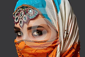 Studio shot of a chrming female wearing the colorful hijab decorated with sequins and jewelry. Arabic style.