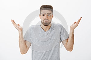 Studio shot of clueless unaware handsome bearded man shrugging with raised hands and eyebrows making silly clueless