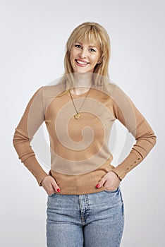 Studio shot of confident blond haired woman wearing sweater and cheerful smiling at isolated background