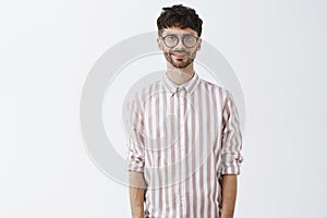 Studio shot of confident good-looking and stylish male model with beard in trendy glasses and striped shirt standing in