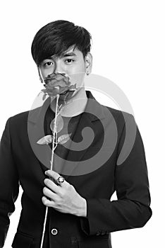 Studio shot of cool handsome Asian businessman smelling red roses