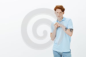 Studio shot of cute redhead gay model with freckles and tattoos, grimacing from dislike, being disgusted and photo