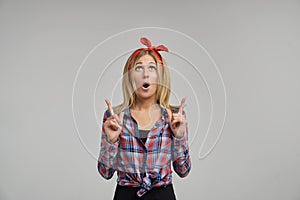 Studio shot of a cute young blonde surprised to open her mouth wide and showing her index fingers up.