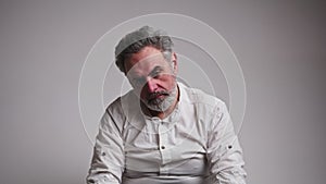 Studio shot of a depressed sad caucasian gray-haired man in his 60s with lowered head looking sadly at camera from time