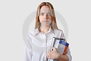 Studio shot of dissatisfied young brown haired woman looking directly at camera, posing over white background, angry girl wearing