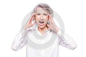 Studio shot of distressed irritated senior woman losing temper screaming out loud from pain and holding hands on head