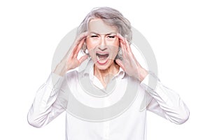 Studio shot of distressed irritated senior woman losing temper screaming out loud from pain and holding hands on head