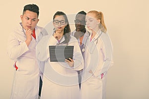 Studio shot of diverse group of multi ethnic doctors thinking while reading on clipboard together