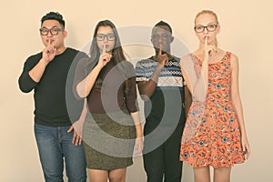 Studio shot of diverse group of multi ethnic friends with finger on lips while wearing eyeglasses together