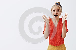 Studio shot of emotive and joyful girl seeing something tremendous waving raised palms smiling broadly and gazing at