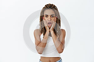 Studio shot of emotive shocked and stunned young dark-skinned cool woman with yellow dreads opening mouth from amazement