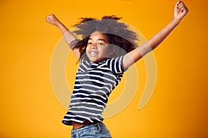 Studio Shot Of Energetic Boy Jumping In The Air With Outstretched Arms Against Yellow Background