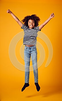 Studio Shot Of Energetic Boy Jumping In The Air With Outstretched Arms Against Yellow Background