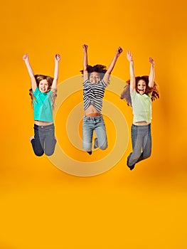 Studio Shot Of Energetic Children Jumping In The Air With Outstretched Arms On Yellow Background