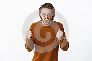 Studio shot of expressive good-looking european bearded guy in sweater and glasses yelling with fure and rage clenching